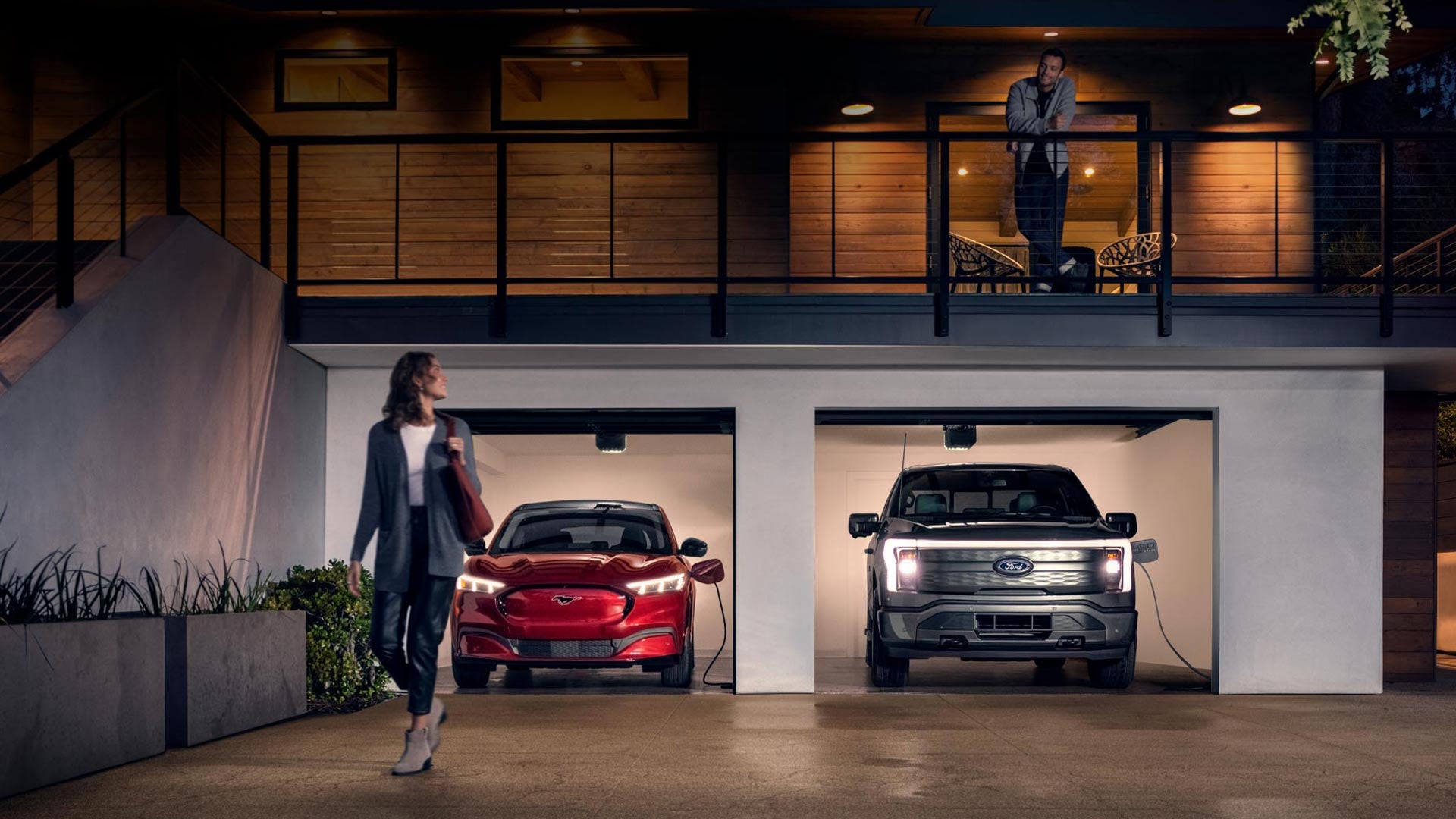 Woman walking out from home garage with a 2024 Mustang® Mach-E and Ford Lightning® truck in plugged-in and charging | Cavalier Ford at Chesapeake Square in Chesapeake VA